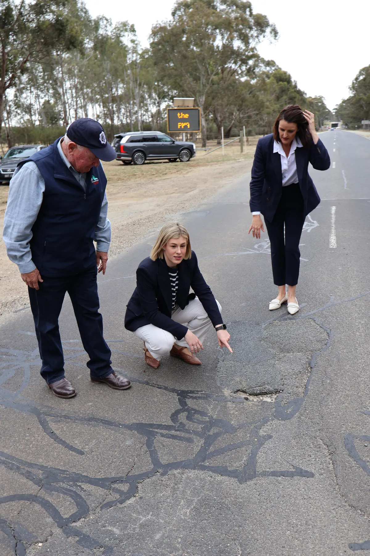 Jess Wilson crouches beside potholes on a country road with local emergency volunteers