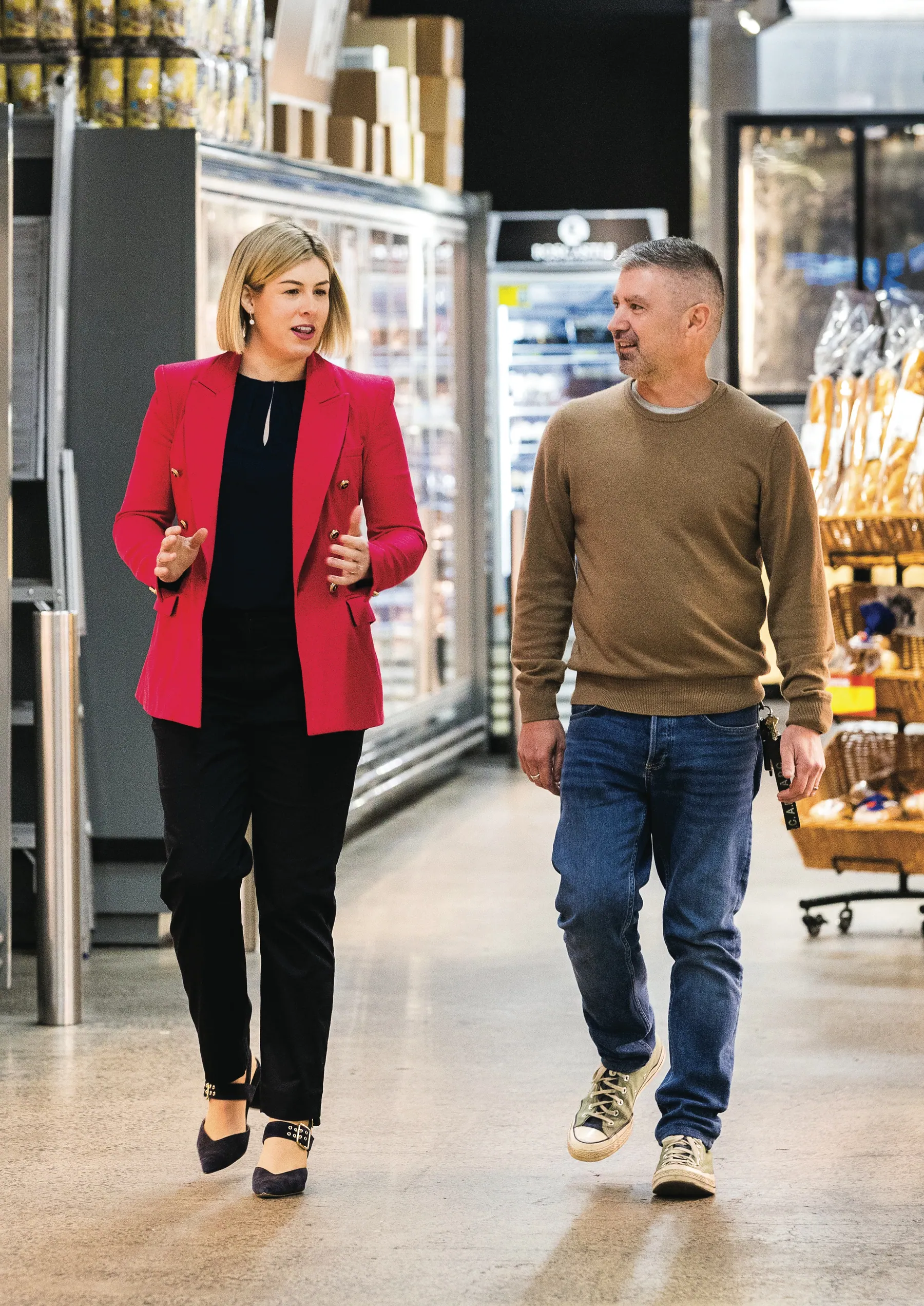 Jess Wilson walks through a supermarket aisle talking with a shopper